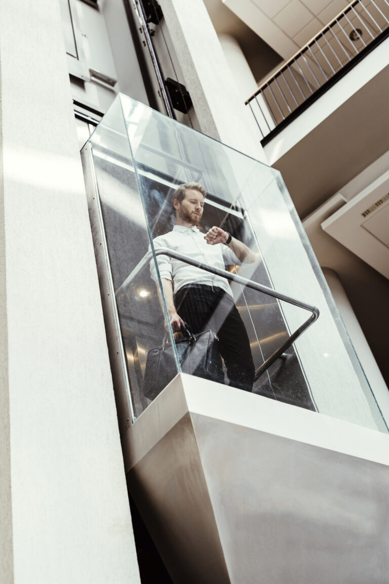 Businessman taking modern glass elevator to the upper floors